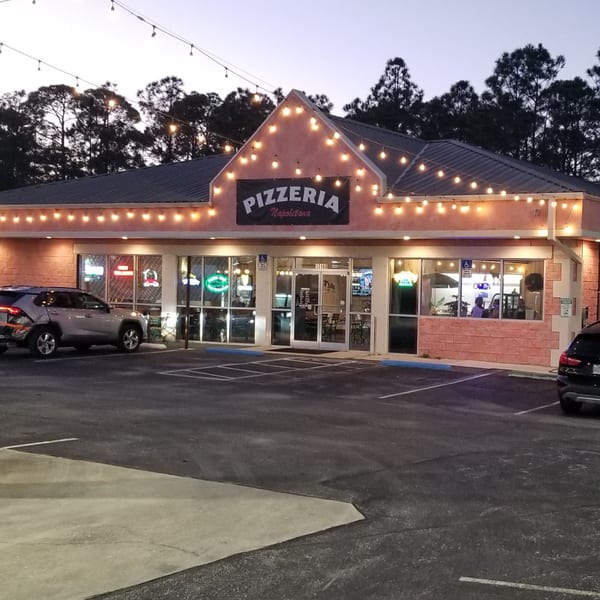 Pizzaluté pizzeria exterior at dusk, with string lights illuminating the building and parking lot.