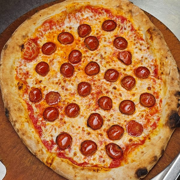 A freshly baked Pizzaluté pepperoni pizza with melted cheese and a crispy crust on a wooden peel.