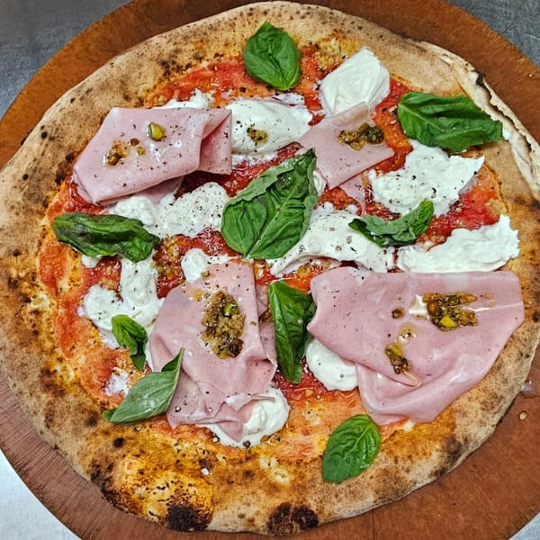 Pizzaluté pizza with mortadella, burrata, basil, and pistachio pesto on a wooden board.