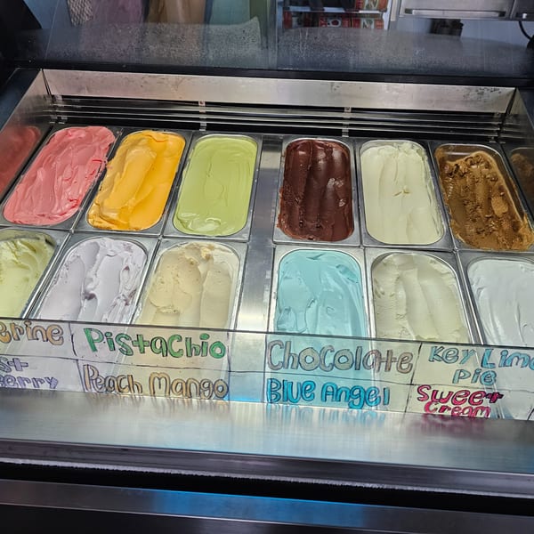 A display case filled with various flavors of gelato, including pistachio, chocolate, and peach mango.