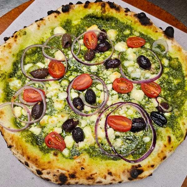 Pizzaluté pesto pizza with cherry tomatoes, black olives, red onions, and feta cheese.