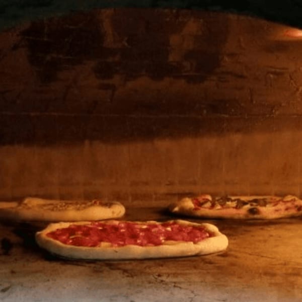 Three Pizzaluté pizzas baking inside a glowing brick oven.