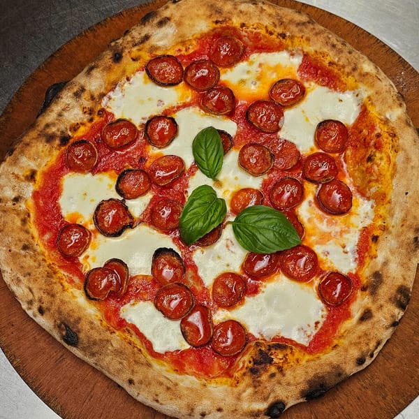 Pizzaluté pepperoni pizza with fresh mozzarella, tomato sauce, and basil on a wooden board.